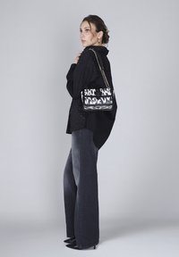Borsa a tracolla in bianco e nero con motivo a catena, forma rettangolare, texture liscia, abbinata a una camicia nera e jeans a gamba larga grigi.