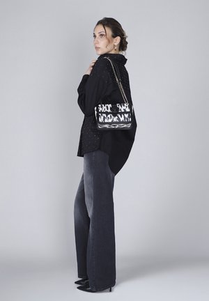 Zwart-wit gestreepte handtas met een kettingband, rechthoekige vorm, gladde textuur, gecombineerd met een zwarte blouse en grijze wijde jeans.