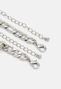 Cadenas de metal plateado con estilos de eslabones variados; incluye eslabones más grandes, eslabones circulares más pequeños y cierres de garra de langosta.