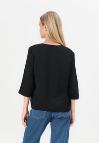 Svart, teksturert topp med trekvartlange ermer og rund hals, kombinert med høyhåndt høyre jeans. Enkelt, moderne design.