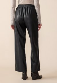 Black faux leather pants with a wide-leg design, elastic waistband, and smooth texture, paired with black heeled ankle boots.