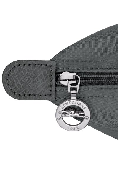 Gray fabric bag zipper with black leather pull tab and silver circular Longchamp logo featuring a galloping horse and the year 1948.