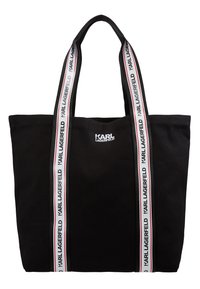 Černá plátěná taška přes rameno. Má dvě ucha s bílým a červeným potiskem "KARL LAGERFELD" po stranách. Jednoduchý obdélníkový design.