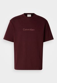 Burgundy cotton t-shirt with a round neck, short sleeves, and subtle Calvin Klein logo in light pink at the center. Smooth texture.