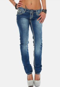 Jean en denim bleu avec une coupe slim, des coutures embellies le long des coutures et un léger effet usé. Assortis à des chaussures à plateforme argentées.