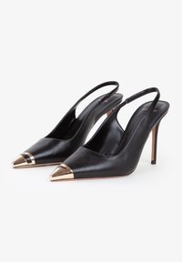 Zapatos de tacón de cuero negro tipo slingback con punta afilada, puntera dorada metálica y acento en la parte delantera, con un tacón alto y esbelto.