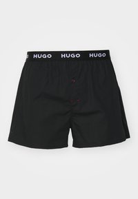 Boxeri negri cu talie elastică, prezentând logo-ul alb "HUGO". Buton roșu în față, design simplu și textură fină.