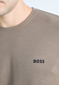 Barna bordázott pulóver, amely kerek nyakkal és egy kis fekete "BOSS" logóval díszítve van a bal mellrészen.