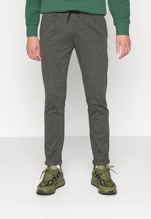 Grå træningsbukser med snor i taljen og tapered ben. Båret med sorte og grønne sneakers med teksturerede detaljer og snørebånd.