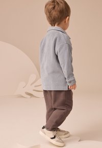 Chemise en velours côtelé bleu clair à manches longues avec un col et des accents de boutons, assortie à un pantalon de survêtement gris et des baskets beige.