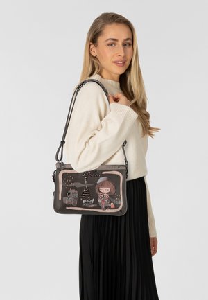 Geprinte schoudertas met een donkere basis en illustraties van Parijse bezienswaardigheden, een personage en tekst. Materiaal is glad met een stevige schouderband.