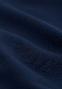 Tessuto blu scuro con una trama fine, liscia e lavorata a maglia con pieghe morbide che creano ombre e riflessi delicati.