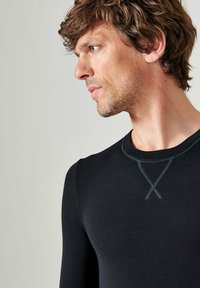 Zwarte langemouwshirt met een ronde halslijn en contrasterende stiksels. De stof lijkt soepel, aansluitend en lichtgewicht te zijn.