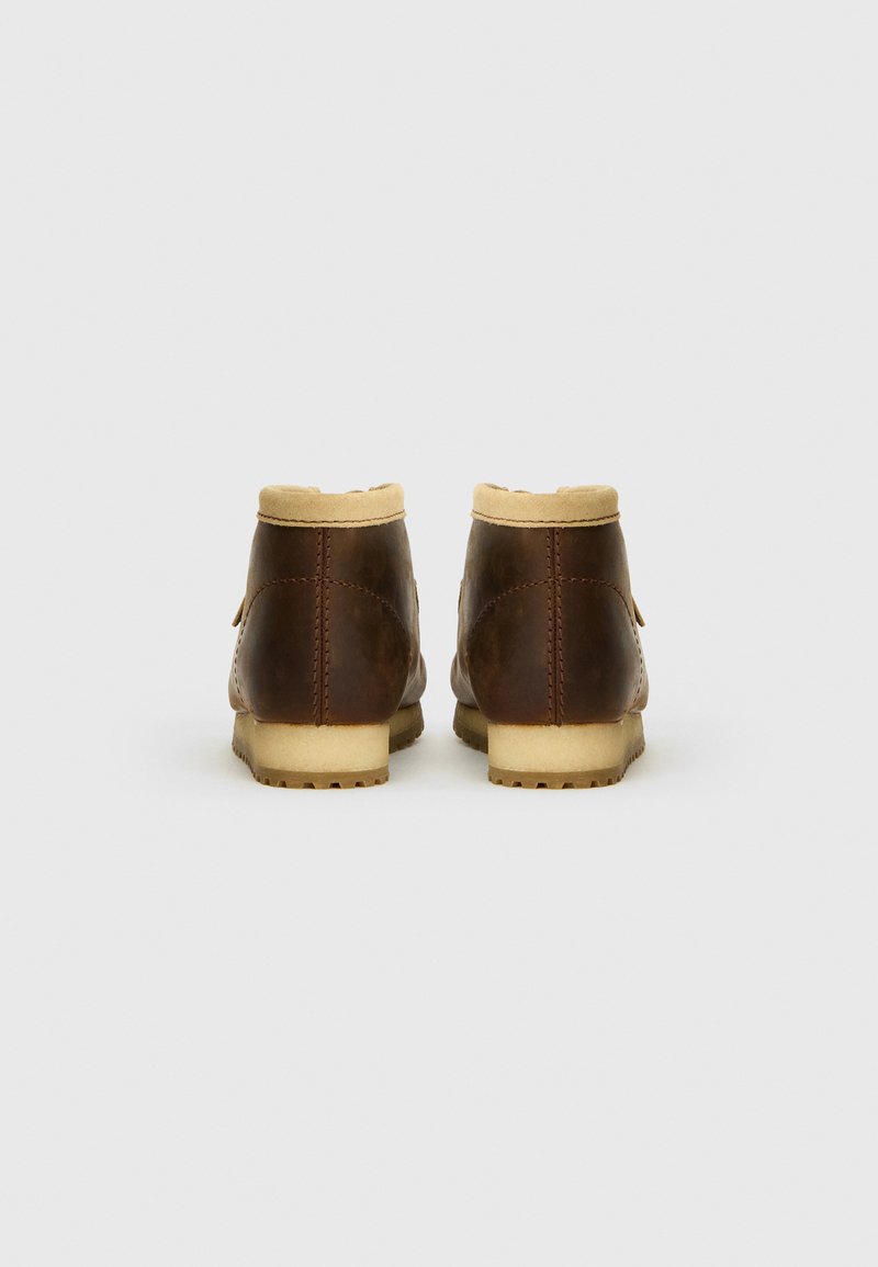 Bottines en cuir marron avec une doublure en fausse fourrure beige, forme arrondie et semelle texturée. La vue arrière montre la couture et des détails en quincaillerie minimalistes.