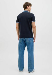 Marineblauw poloshirt met blauwe accentstrepen op de kraag en mouwen, gecombineerd met lichtblauwe rechte jeans. Katoenen stof, casual pasvorm.