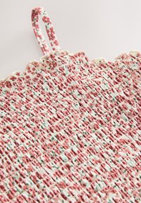 Sac en tissu tissé présentant un motif floral rose sur fond blanc, avec une surface texturée et une petite anse pour le transport.