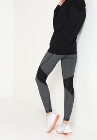 Leggings ajustados grises con paneles de malla negra, hechos de material elástico, combinados con una sudadera negra y zapatillas deportivas blancas.