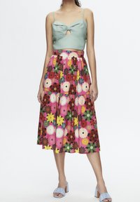 Lichtgroene crop top met een strikdetail, gecombineerd met een roze tiered rok met levendige bloempatronen. Blauwe hakken maken de look compleet.