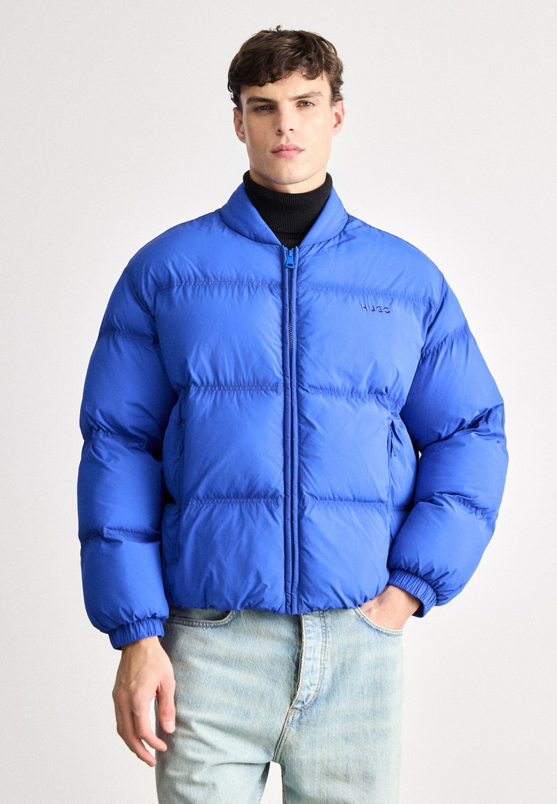 Ryškiai mėlynas pūkinis blynas su stovinčia apykakle, siuvinėta konstrukcija, bangomis siūtos rankoves ir priekiniais užtrauktukais. Išsiuvinėtas logotipas ant krūtinės.