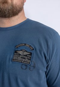 Modré bavlněné tričko s texturovanou výšivkou znaku "Petrol Ind. Co.", retro písmem a emblémem s křídly.