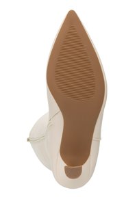 Zool van een spits toelopende beige laars met een getextureerde bruine rubberen zool en een klein patroon op de hielpunt, gefotografeerd van onderen tegen een witte achtergrond.