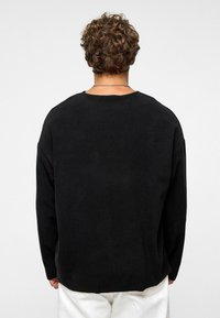 Zwarte sweatshirt met lange mouwen, losse pasvorm, ronde halslijn, zachte textuur. De achterkant toont een minimalistisch ontwerp met een licht gebogen zoom.