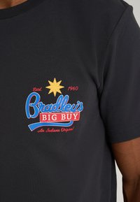 Black cotton t-shirt featuring a central logo with a yellow star, blue and red text stating "Bradley's BIG BUY," established 1960.