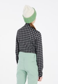 Chemise noire à manches longues avec un motif pied de poule gris, pantalon taille haute vert clair, bonnet en tricot crème et vert.