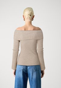 Haut côtelé, à épaules dénudées en beige, corsage ajusté, manches longues, tissu texturé. Associé à un jean large bleu clair.
