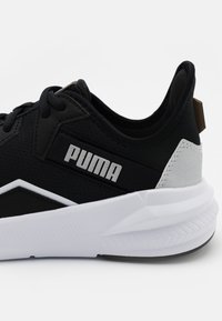 Mustat urheilukengät, joissa on verkkopinta, PUMA-logo, valkoinen välipohja ja teksturoitu ulkopohja. Korostettu harmaalla kantapään yksityiskohdalla.