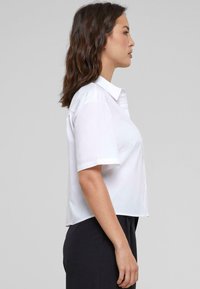 Lühikeste varrukatega valge särk, kaelusega, kitsas istuvus, valmistatud siledast kangast, sirge äär ja minimalism.