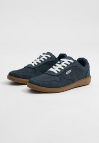 Zapatillas de lona azul marino con cordones blancos, suela de goma, punta redondeada y detalles de costura sutiles. Presenta una etiqueta de la marca en el lateral.