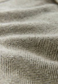 Light beige fabric with a textured herringbone pattern. The material appears soft and plush, with visible ridges and depth in folds.
