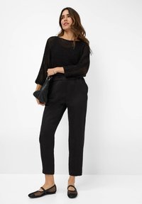 Zwarte mesh trui met brede mouwen, gecombineerd met hoge taille zwarte broek. Een zwarte handtas met textuur completeert de look, met mesh slippers.
