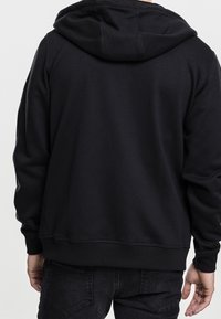 Felpa nera con cappuccio, dotata di polsini e orlo a costine. Presenta una texture semplice e liscia e una vestibilità comoda e rilassata, progettata per il massimo comfort.