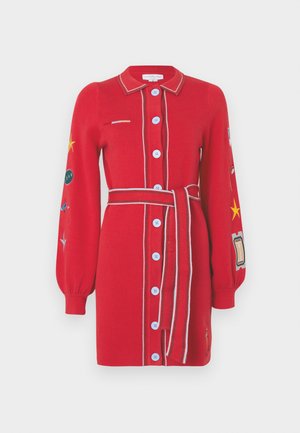 Czerwona dzianinowa sukienka z zapięciem na guziki, długimi rękawami, pasiastym kołnierzykiem i paskiem w talii. Posiada wyszywane naszywki oraz kontrastujące niebieskie guziki.