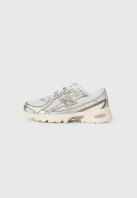 Valkoinen ja beigekiloinen New Balance 740 -kengät, joissa on verkkokangas, nauhakiristyksellä etuosa ja pehmustettu pohja, yksinkertaisella valkoisella taustalla.