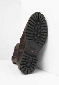 Stivale in pelle marrone con suola in gomma nera testurizzata caratterizzata da scanalature profonde per una buona trazione e un logo. Dettaglio della fascia laterale visibile.