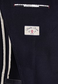 Innenansicht eines marineblauen Blazers mit Gewebestruktur und Savile Row-Etikett. Verfügt über kontrastierende weiße Nähte, mehrere Taschen und ein kariertes Futter.