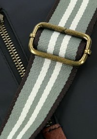 Schwarze Stofftasche mit einem Metallreißverschluss, einem grau-weißen gestreiften Riemen und einer Messingschnalle mit braunen Lederakzenten.