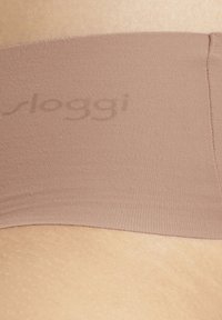 Bande en tissu brun clair, texture lisse, présentant le logo « sloggi » subtil. Gros plan sur la ceinture élastique et la peau en dessous.