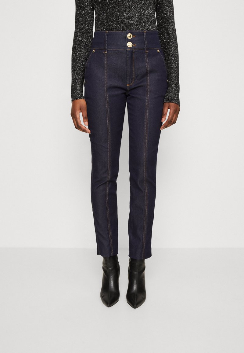 Höga mörka denimbyxor har två gyllene knappar i midjan, kontrasterande orange sömmar och en slim fit med ankellång längd.