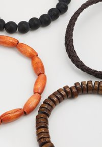 Four bracelets: black round beads, orange oval wood beads, brown braided leather, and dark wooden discs in varying thicknesses.