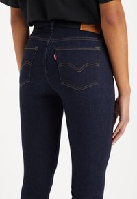 Mörkblå denimjeans med hög midja, synlig sömnad och två bakfickor med en karakteristisk böjd design. Läderlogotyp på midjebandet.