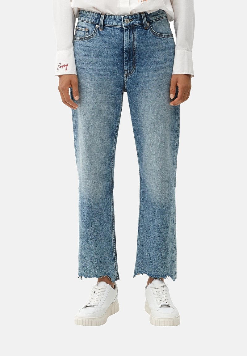 Jeans azules de cintura alta con un diseño de pierna recta, dobladillo deshilachado y detalles de desvanecimiento, combinados con zapatillas blancas.