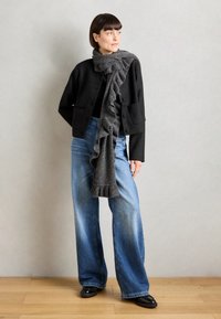 Zwarte cropped jas met twee voorzakken, gecombineerd met een rimpelgrijze sjaal en een wijd model vervaagde blauwe jeans, afgemaakt met zwart schoeisel.