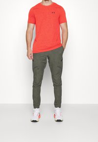 Camisa corta de manga corta con textura roja, pantalones jogger verde olivo con bolsillos laterales y zapatillas blancas con acentos rojos y amarillos.