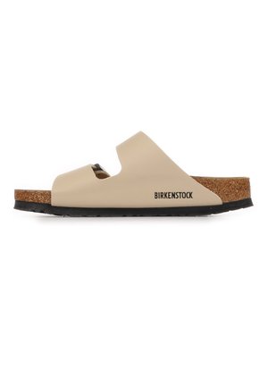 Sandalia tipo chancla Birkenstock en beige con puntera abierta, dos tiras recortadas, plantilla de corcho y suela negra, vista de perfil.