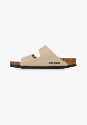 Sandalo beige Birkenstock aperto davanti con due cinturini traforati, plantare in sughero e suola nera, mostrato di profilo.