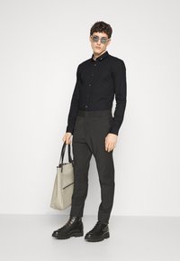 Camisa negra de manga larga, pantalones con cintura elástica en gris oscuro, botas negras con cordones y un bolso de tote gris claro con asas negras.